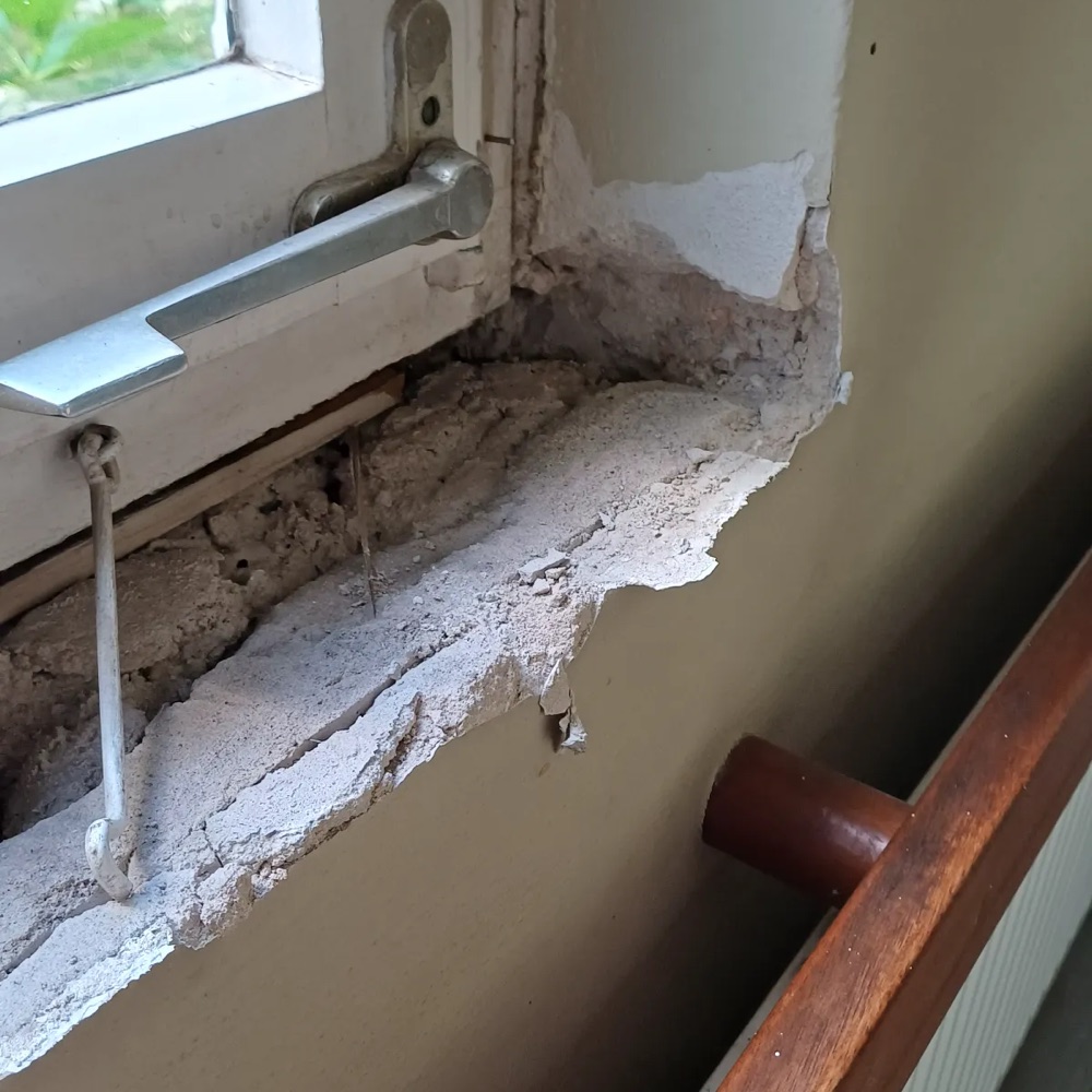 Flurfenster ohne Fensterbank: offenes M&ouml;rtelbett mit losen Bruchst&uuml;cken unter dem Fensterrahmen